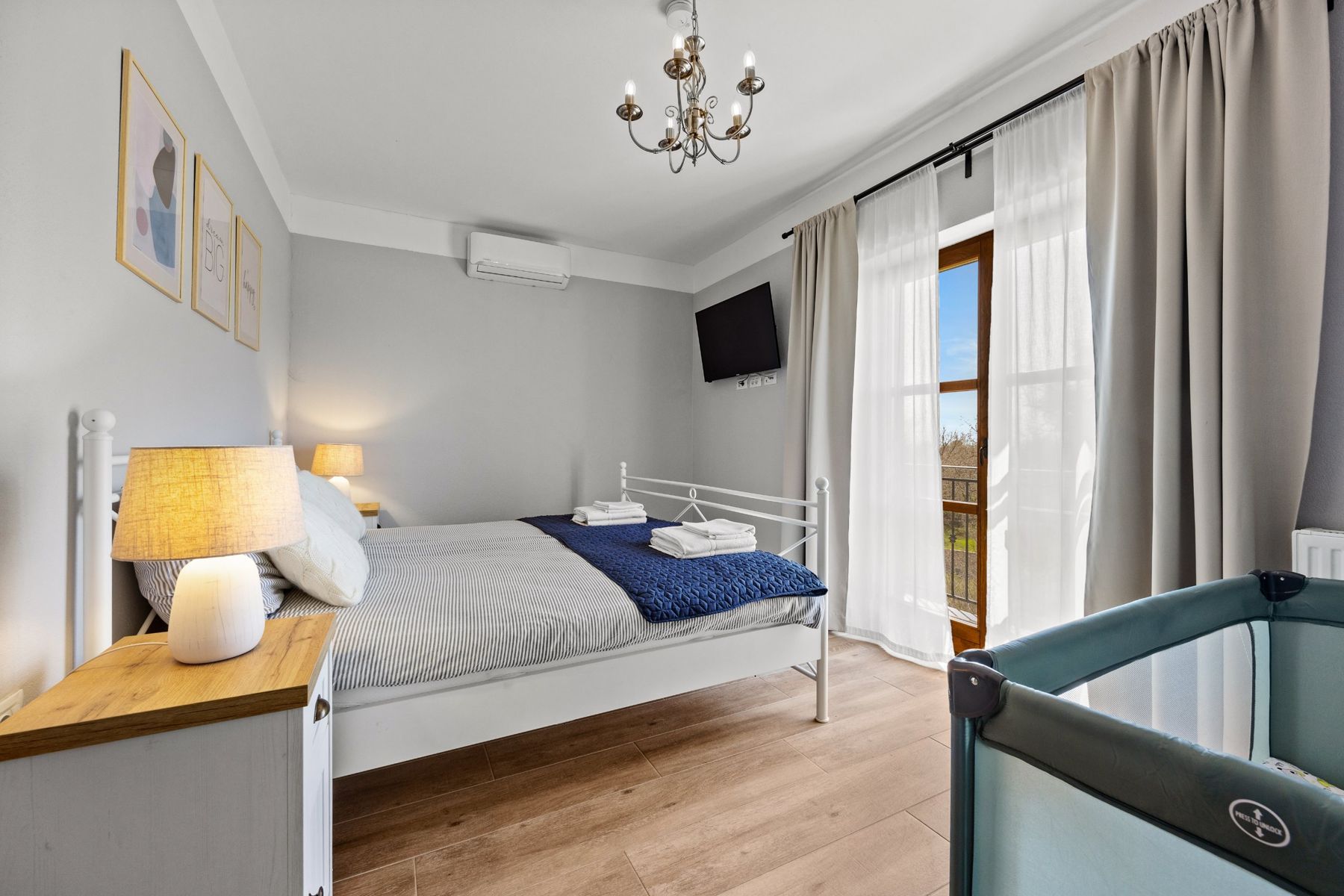 Bright grey bedroom with a double bed, a travel cot and a balcony door