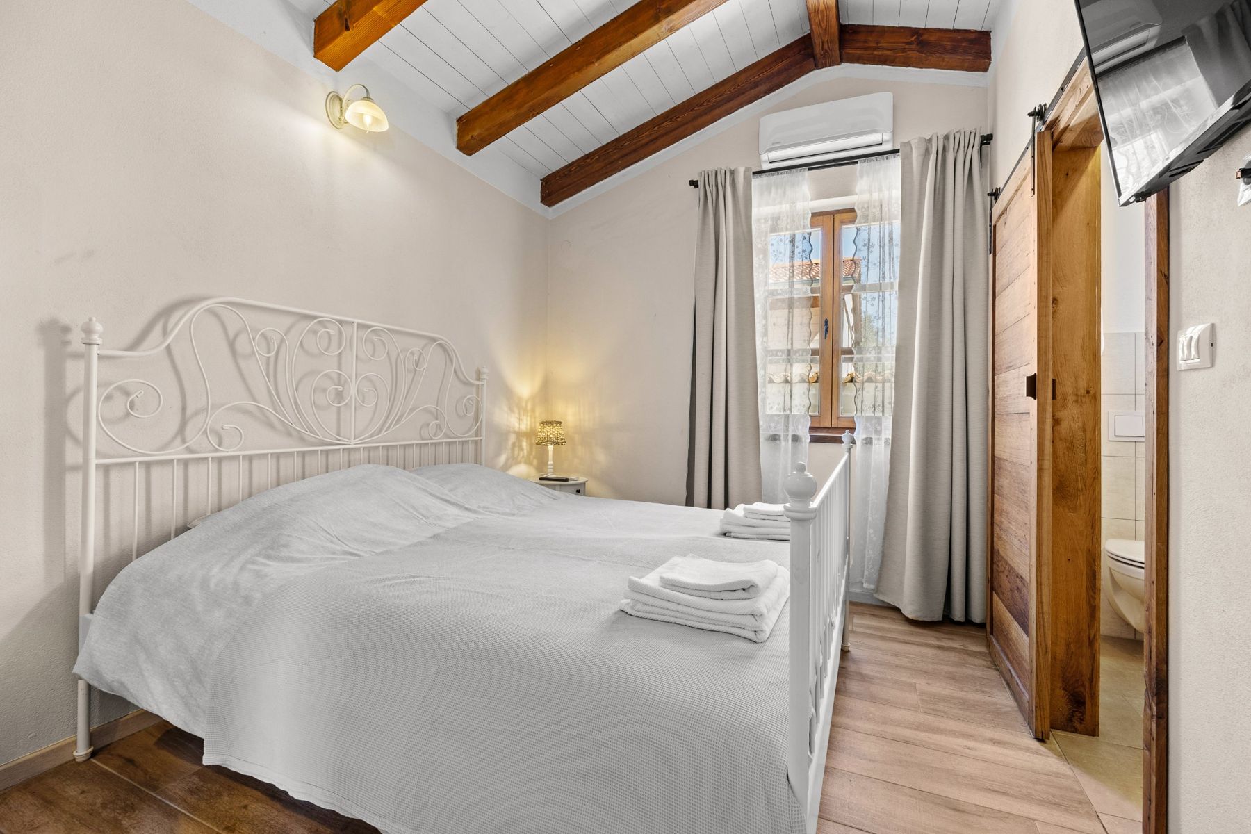 Bedroom with a white metal bed under a sloping ceiling with wooden beams
