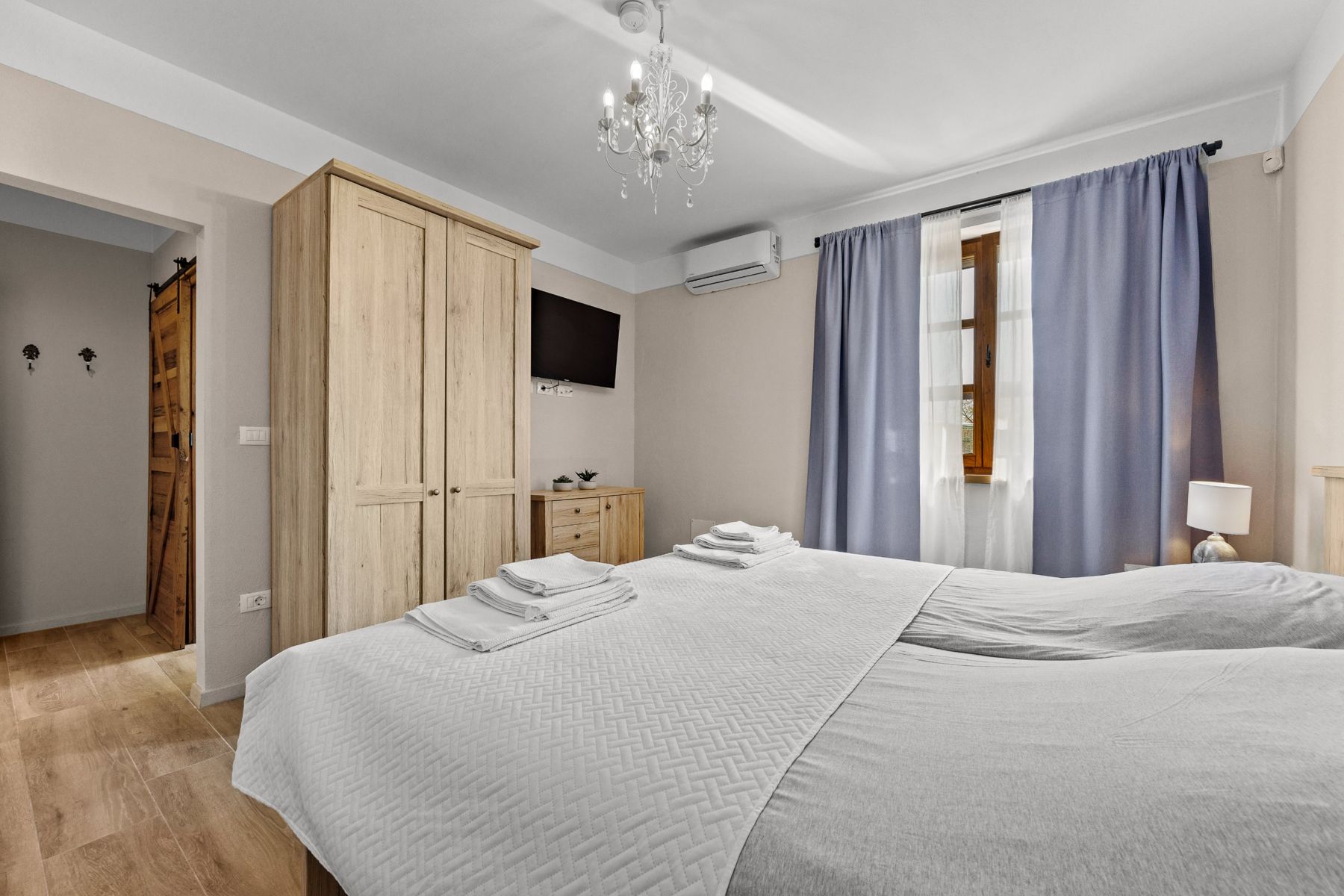 Bedroom with a large bed, wooden wardrobe, TV and blue curtains