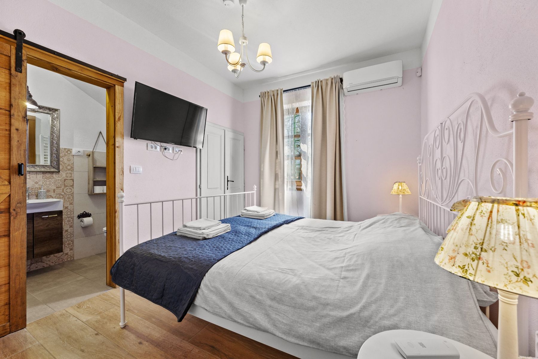 Pink double bedroom with a wall-mounted TV and bathroom behind a sliding wooden door