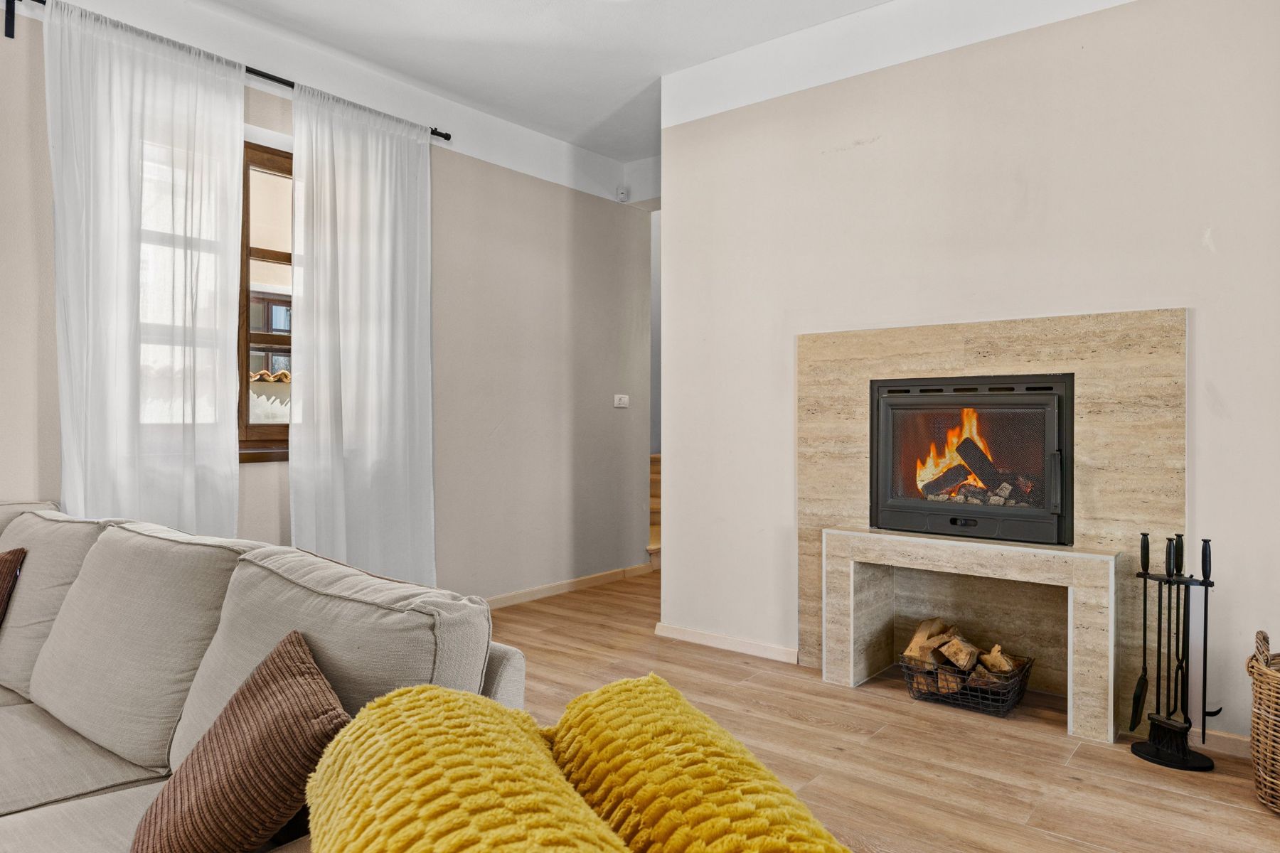 A lit fireplace with a log basket and fireplace tools