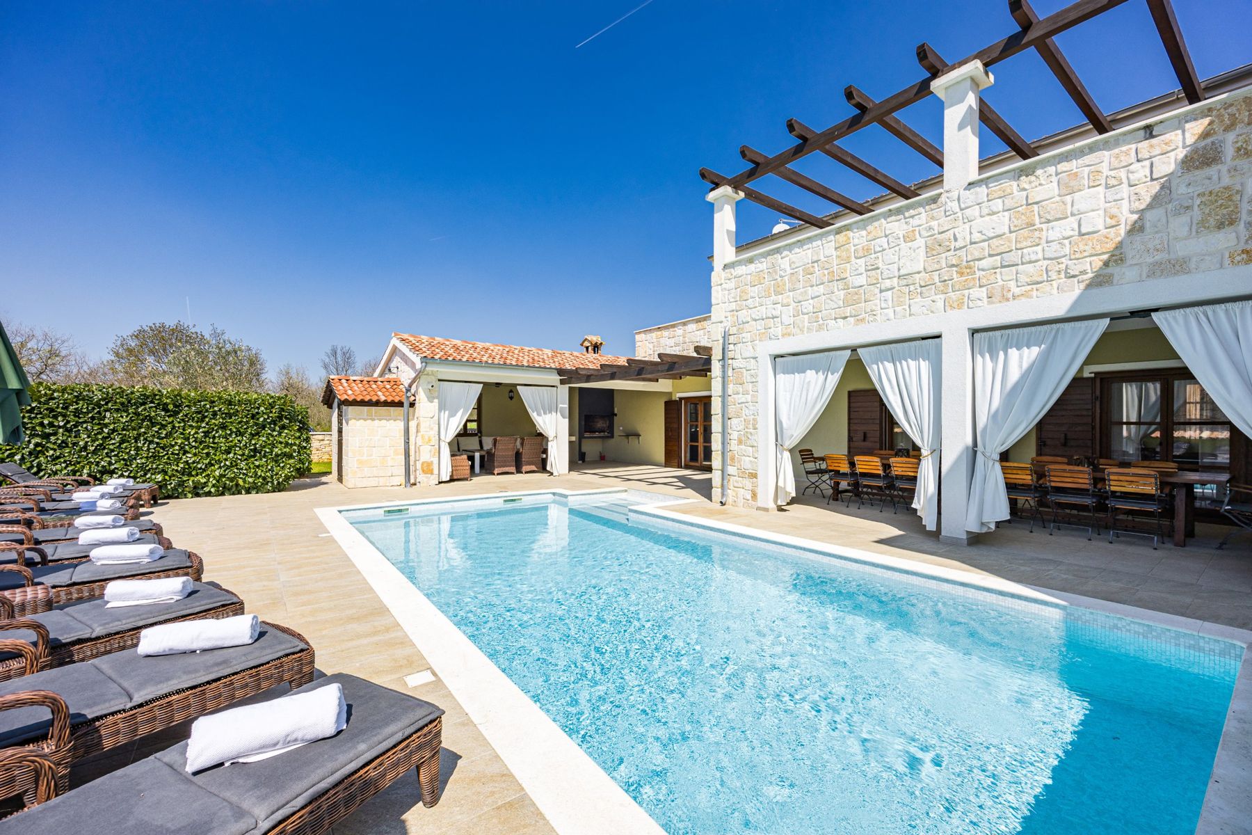 Sun loungers beside the pool, with the covered terrace and outdoor lounge